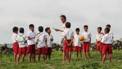 A teacher and schoolchildren playing together on a grassy field