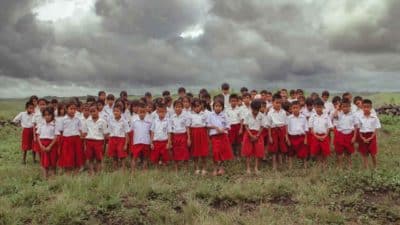Schoolchildren in red and white uniforms standing together on a grassy field