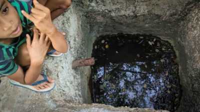 A child beside a shallow concrete well containing dark water