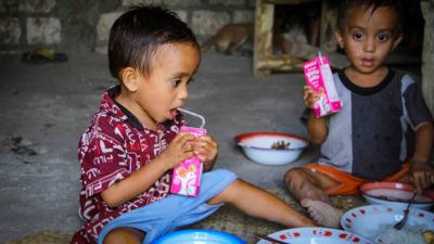 Two young children with bowls and drink cartons inside a home