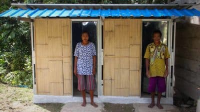Two residents standing in the doorways of a sanitation building with a blue roof