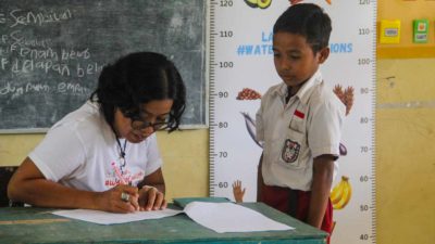 A health worker recording a schoolboy's measurements beside a height chart