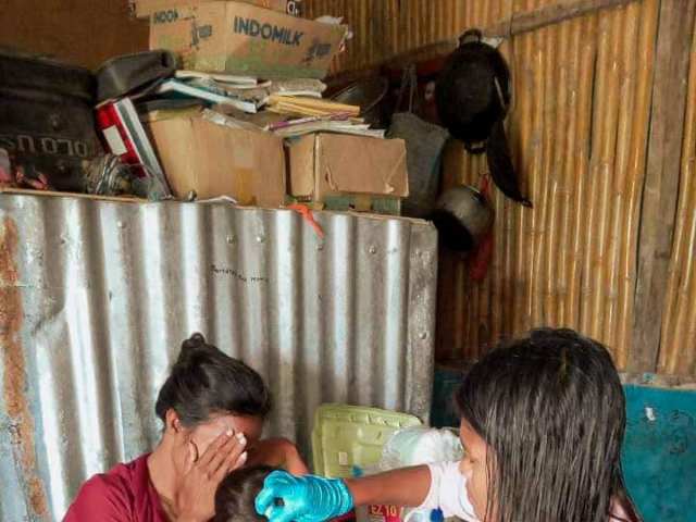 A health agent from Kawan Sehat is providing medical care to a patient in a remote village.