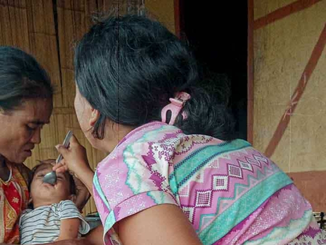 A health agent from Kawan Sehat is providing medical care to a patient in a remote village.