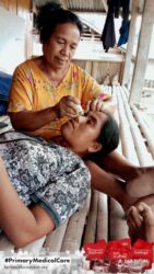A health agent from Kawan Sehat is providing medical care to a patient in a remote village.