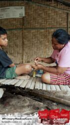 A health agent from Kawan Sehat is providing medical care to a patient in a remote village.