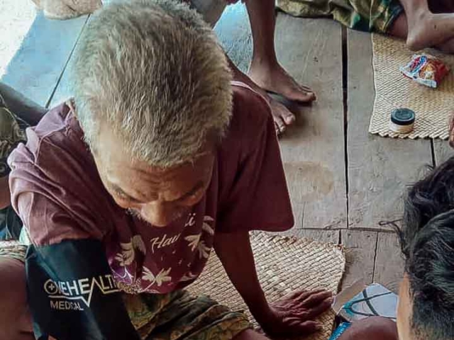 A health agent from Kawan Sehat is providing medical care to a patient in a remote village.