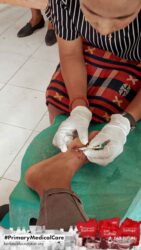 A health agent from Kawan Sehat is providing medical care to a patient in a remote village.