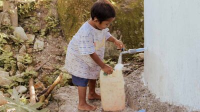 Rural child collecting clean water from a ferrocement reservoir, symbolizing health and hope.