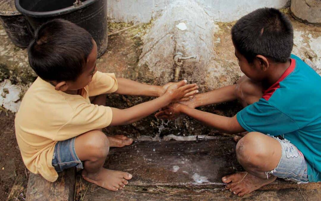 Children washing hands with clean water from a ferrocement reservoir in a rural village.