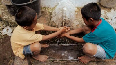 Children washing hands with clean water from a ferrocement reservoir in a rural village.