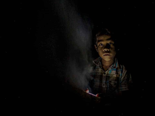 Children in East Sumba studying by the light of a SolarBuddy lamp, seated on the floor of their wooden home, deeply focused on their homework.