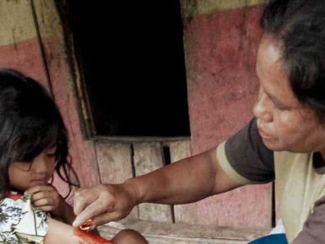 A health agent from Kawan Sehat is providing medical care to a patient in a remote village.