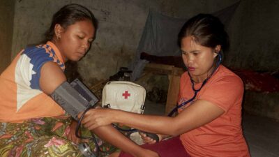 A health worker checking a woman's blood pressure beside a medical backpack