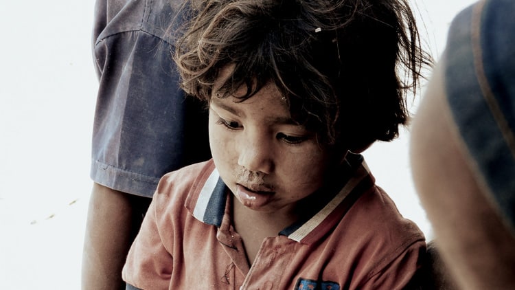 Children in rural Indonesia carrying water containers through dry, dusty paths to their home