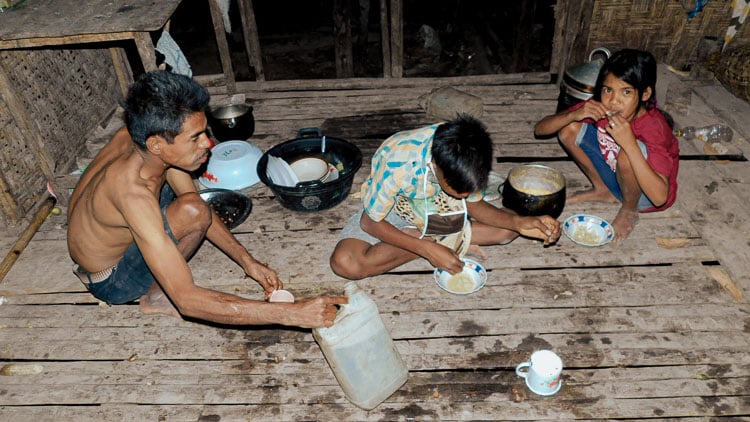 Family in a wooden house using unsanitary water to cook and eat on the floor.