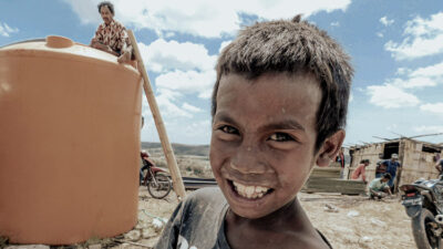Children carrying water containers on foot in rural Indonesia, facing tough living conditions without access to clean water