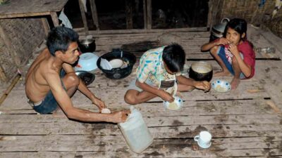 Children in rural Indonesia carrying water containers through dry, dusty paths to their home