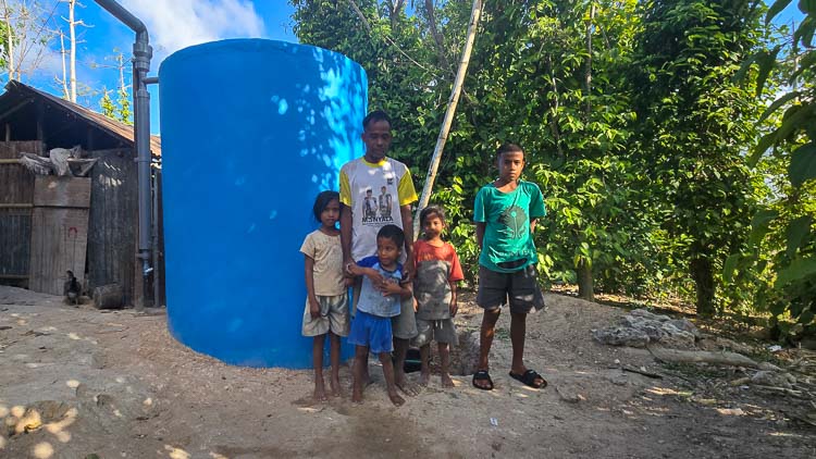 Une famille se tient devant un nouveau réservoir d’eau en ciment de 5 350 litres, construit par Fair Future à Hambarita pour améliorer l’accès à l’eau potable et la santé des enfants vivant dans ce village isolé de l’Est indonésien.