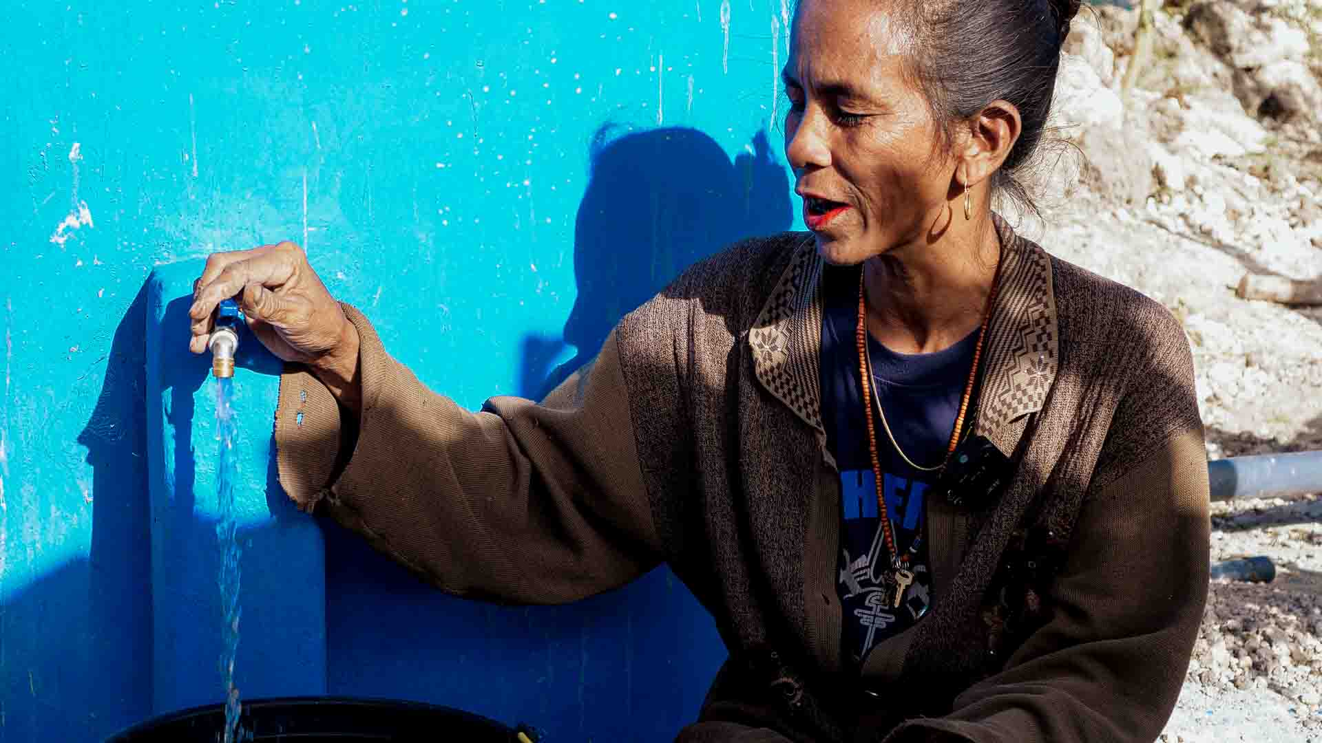 Hambarta woman opening a tap connected to a new ferrocement rainwater tank, part of Fair Future’s clean water project.