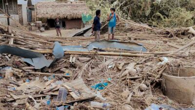 Two men standing among flood debris and a destroyed home, showing the impact of extreme weather on health and living conditions