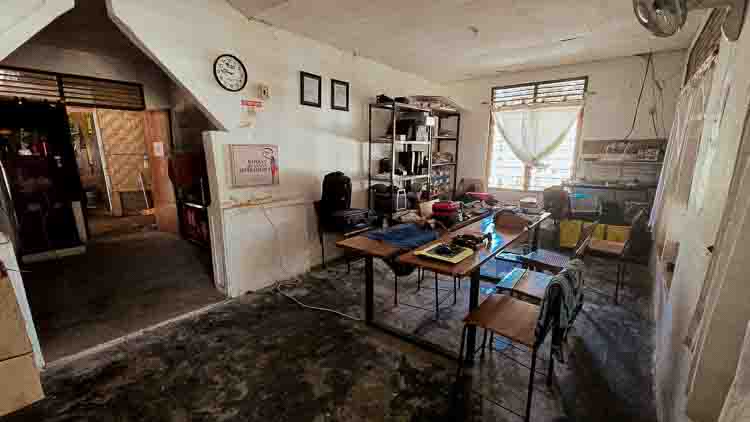 Le bureau de Rumah Kambera, épuisé par le terrain Petit bureau vétuste à Rumah Kambera, avec tables, chaises, étagères chargées de matériel et sol très abîmé, où l’équipe de Fair Future organise ses missions.