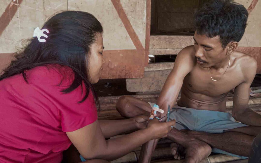 Health agent cleaning and dressing a forearm cut in a rural house