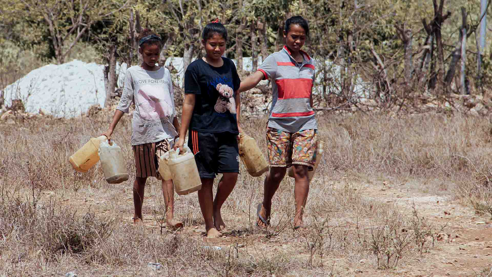 Three girls walking across dry ground carrying jerrycans of water, illustrating climate change and health impacts