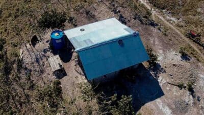 Aerial view of a lone house and the blue Wai Pa Luri Wangu rainwater tank in a remote, arid landscape of East Sumba.