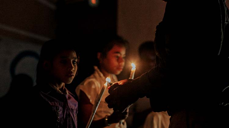 Des enfants tiennent des bougies allumées lors d’une fête de Noël dans un village sans électricité, éclairant leurs visages dans l’obscurité.