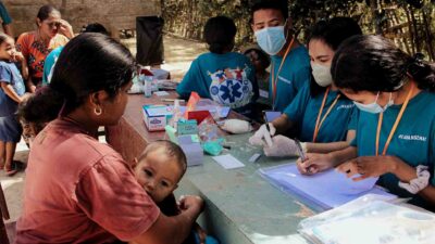 A health worker performs a malaria rapid diagnostic test for a child beside their mother in rural East Sumba