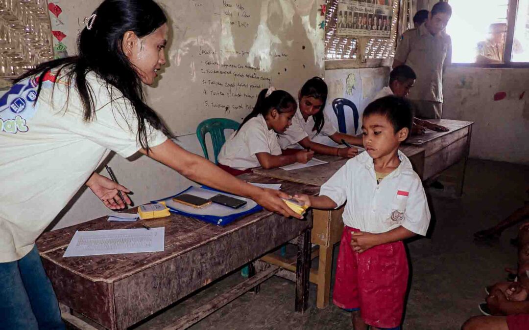 A Fair Future collaborator hands a SolarBuddy lamp to a young student inside an ultra-rural school classroom in East Sumba, Indonesia.
