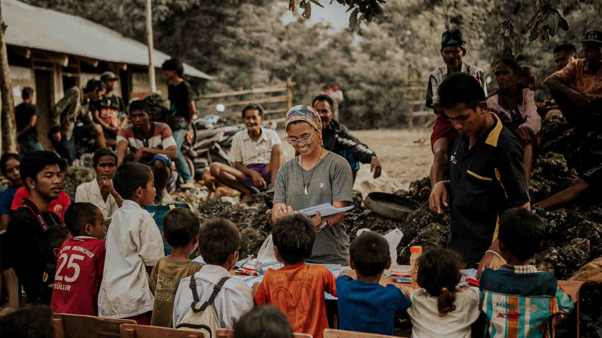 Children and families in a remote East Sumba village studying outdoors, drawing, carrying desks, dancing and sharing food as part of community based education and empowerment activities.