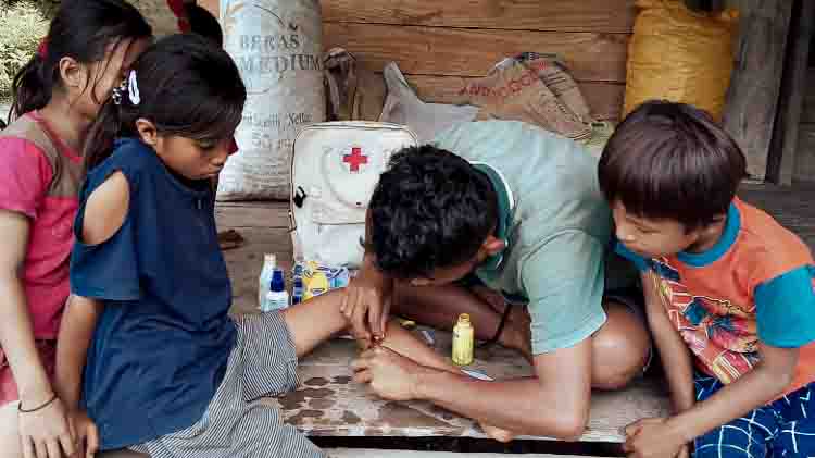 Un agent de santé de Kawan Sehat nettoie une plaie à la jambe d'un enfant lors d'une visite à domicile dans une zone rurale de l'est de Sumba, en Indonésie.