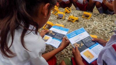 Des enfants indonésiens issus du milieu rural lisent un dépliant d’ SolarBuddy éducation pendant une séance de recharge des lampes.