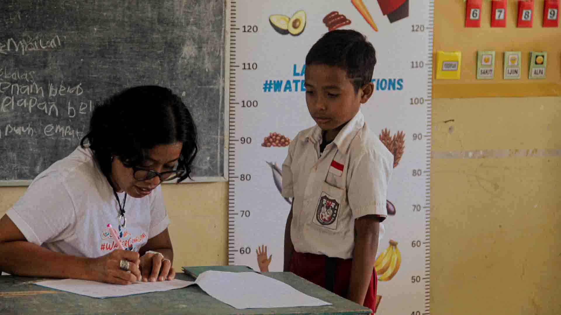 Child undergoing height measurement during rural medical visit in East Sumba to detect malnutrition and immune risk.