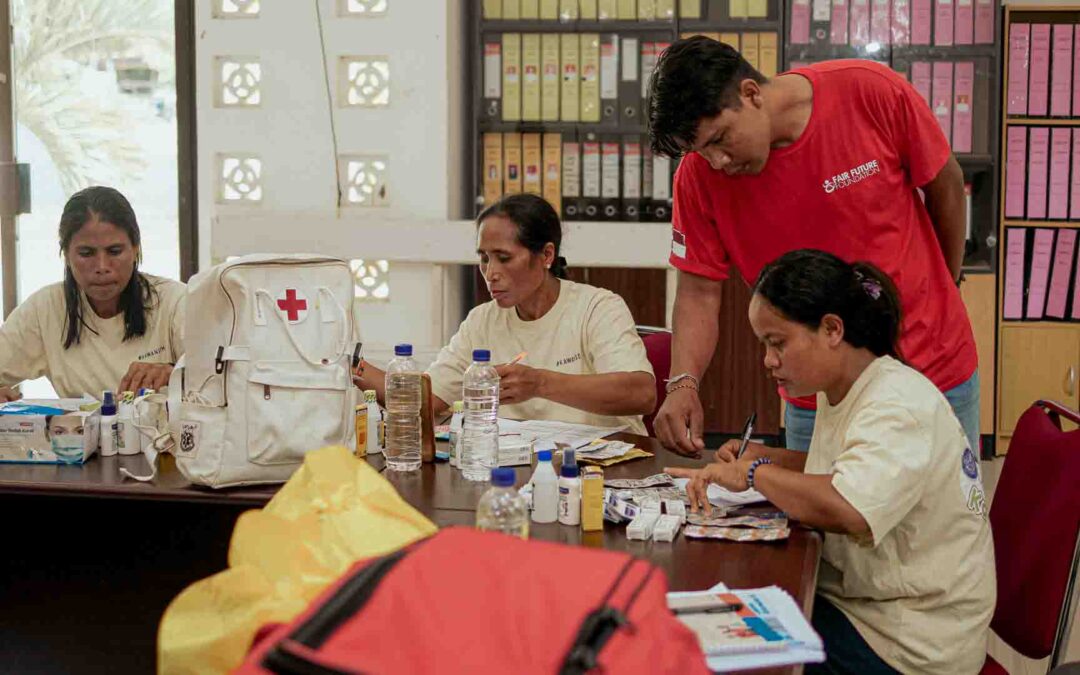 Primary Medical Care supervision meeting at Puskesmas Kawangu in East Sumba, where field coordinator Erwin reviews medical supplies and patient records with Kawan Sehat health agents to ensure essential care in ultra-rural villages.