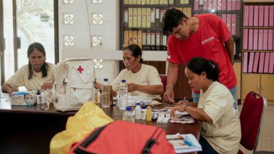 Primary Medical Care supervision meeting at Puskesmas Kawangu in East Sumba, where field coordinator Erwin reviews medical supplies and patient records with Kawan Sehat health agents to ensure essential care in ultra-rural villages.