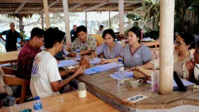 Group of people seated at a wooden table outdoors, discussing papers and taking notes.