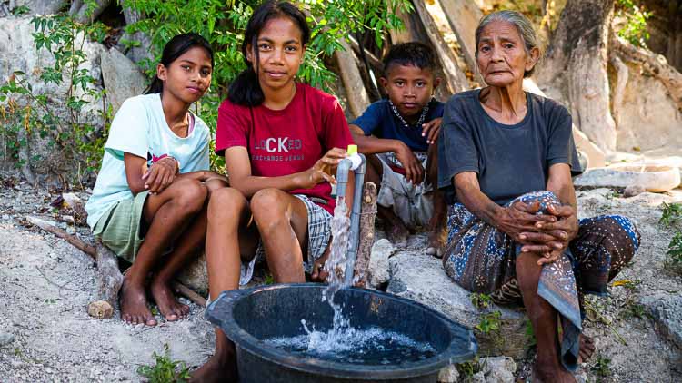 Family in East Sumba sitting beside a water tap connected to a new Fair Future Foundation reservoir