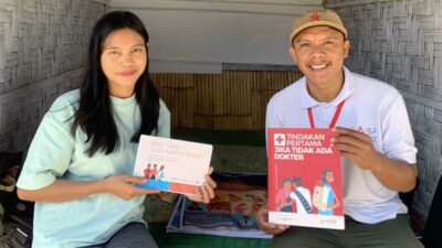 Two people sit in a woven hut, smiling, each holding health information booklets.
