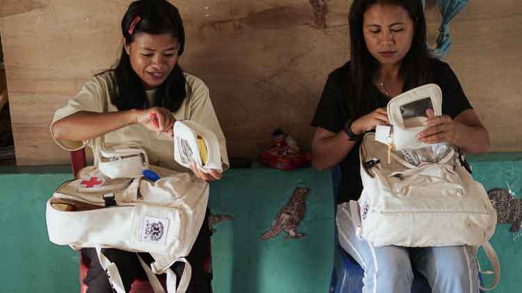 Two Kawan Sehat health agents sitting indoors and preparing white medical backpacks during a primary healthcare training session in East Sumba.