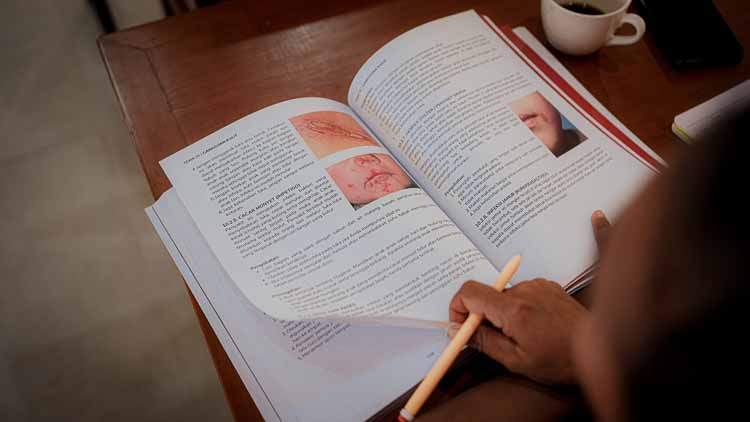 Open Kawan Sehat medical training manual with illustrated clinical modules being reviewed on a table.