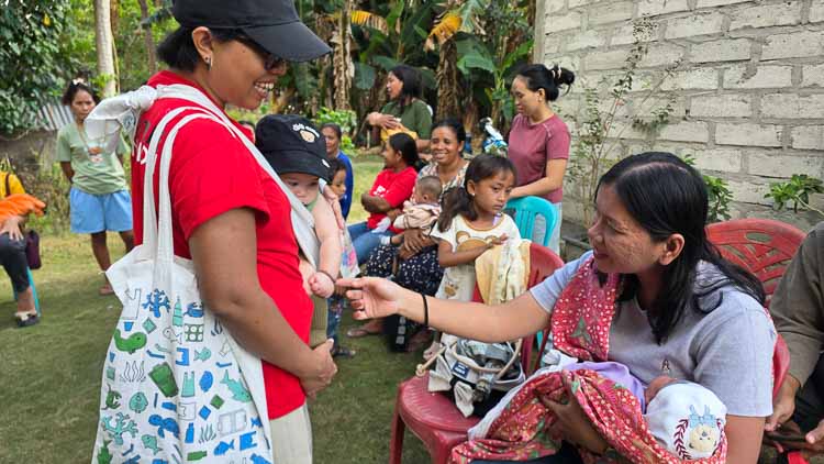 Sorai in a baby carrier surrounded by children and families during a community health check-up day in East Sumba.