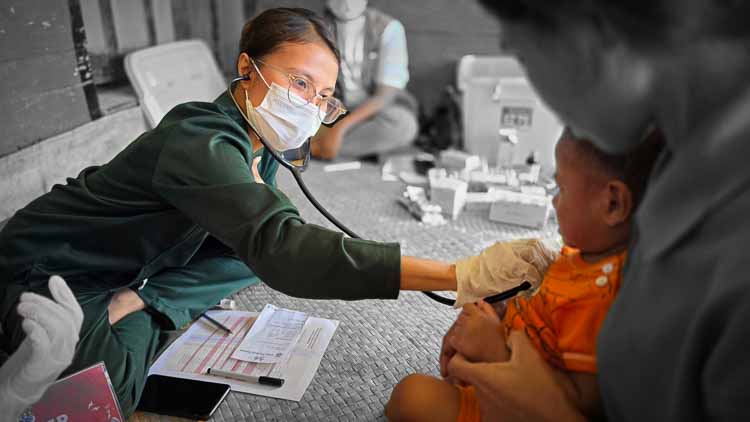 Healthcare worker using a stethoscope to examine a young child during a community medical clinic in rural East Sumba, Indonesia.