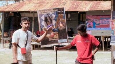 Health worker presents a secondhand smoke prevention poster during community care in Kampung Madutolung.