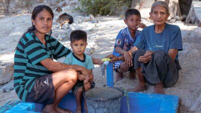 Deux femmes et deux enfants près d'une source d'eau domestique, qui remplissent un seau à partir d'un système d'alimentation en eau par gravité.