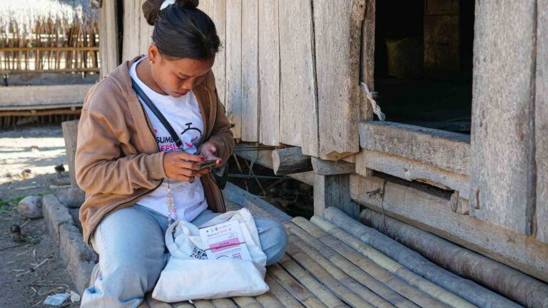 Rambu Fratika Utilisation d'un téléphone pour effectuer des travaux de Sumba Sepsis Study terrain à côté d'une maison en bois dans l'est de Sumba.