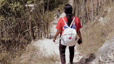 Kawan Sehat community health worker walking through a village with a medical backpack