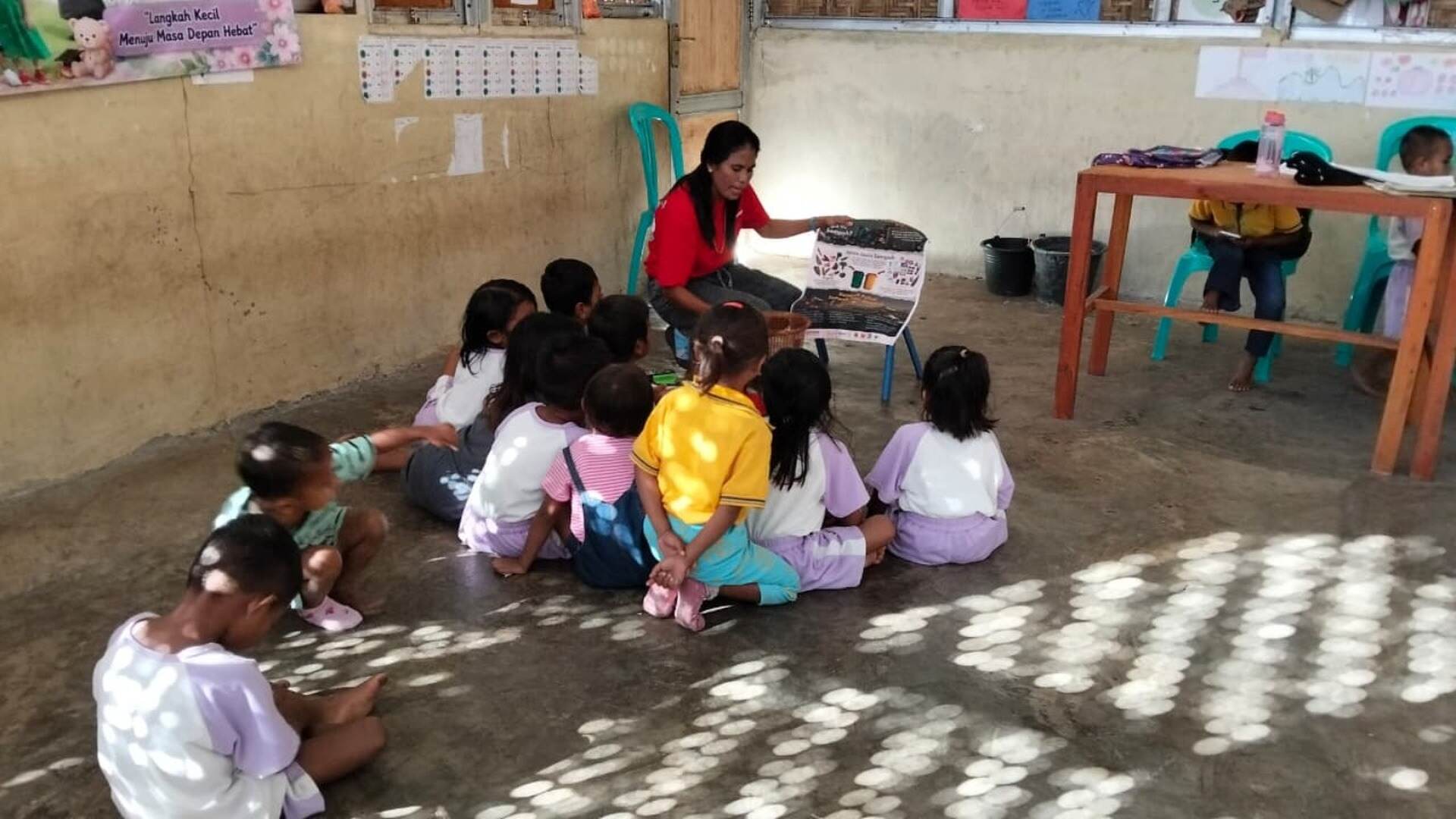 Kawan Sehat health agent teaching young pupils about plastic waste with a hand-drawn poster in East Sumba